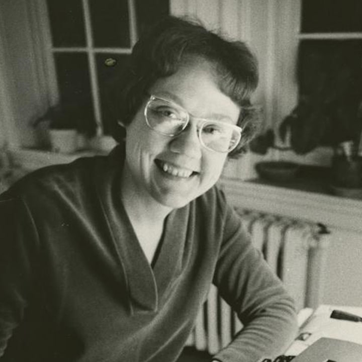 Black and white headshot Barbara Gittings smiling. Her typewriter sits on the desk in front of her.