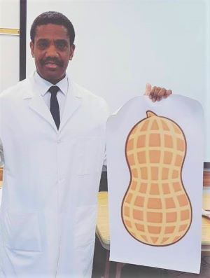 Photograph of Keith Henley as George Washington Caver in a white lab coat holding a drawing of a peanut.