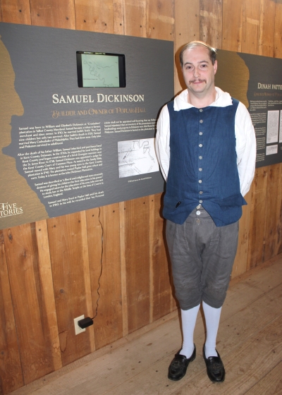 Photo of historic-site interpreter Chris Merrill standing in front of a section of the “Five Stories” display