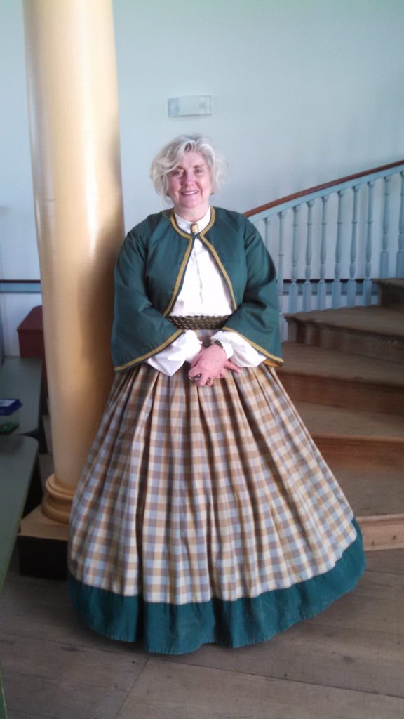 Susan Emory wears green, white and plaid historic clothing for a program.