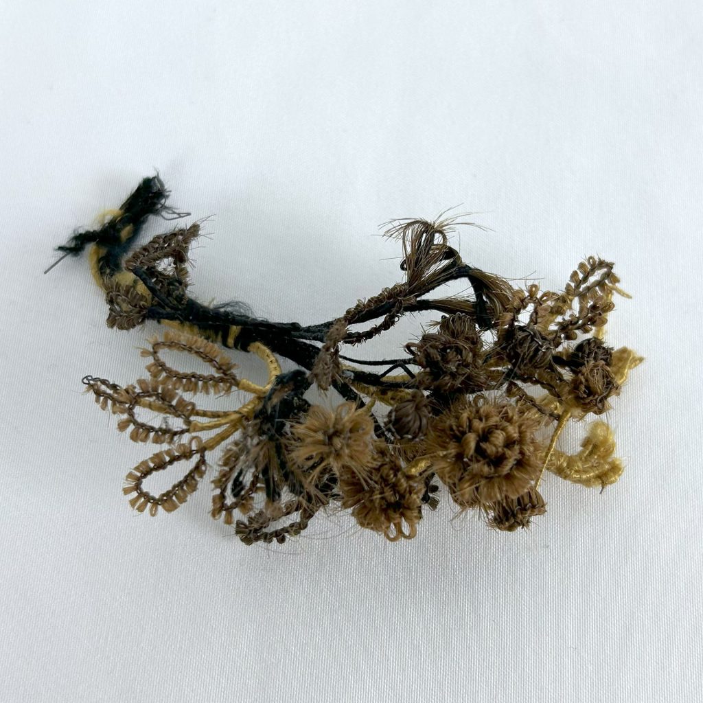An image of a small bouquet of flowers made from human hair, showing different colors of hair from different individuals ranging from blonde to dark brown or black.