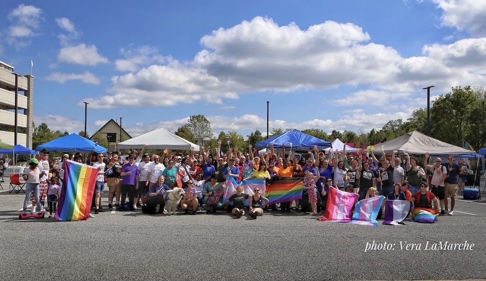 A crowd of youth and adults hold pride flags and cheer in a parking lot.