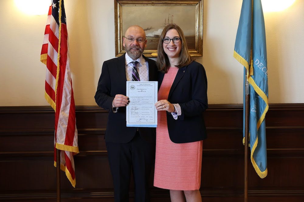 A white man and white woman smile holding a signed bill.