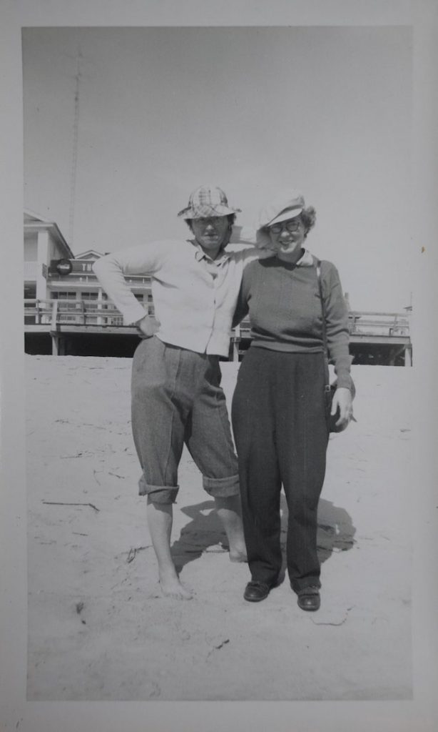 A black and white photograph of two women smiling and standing on the beach.