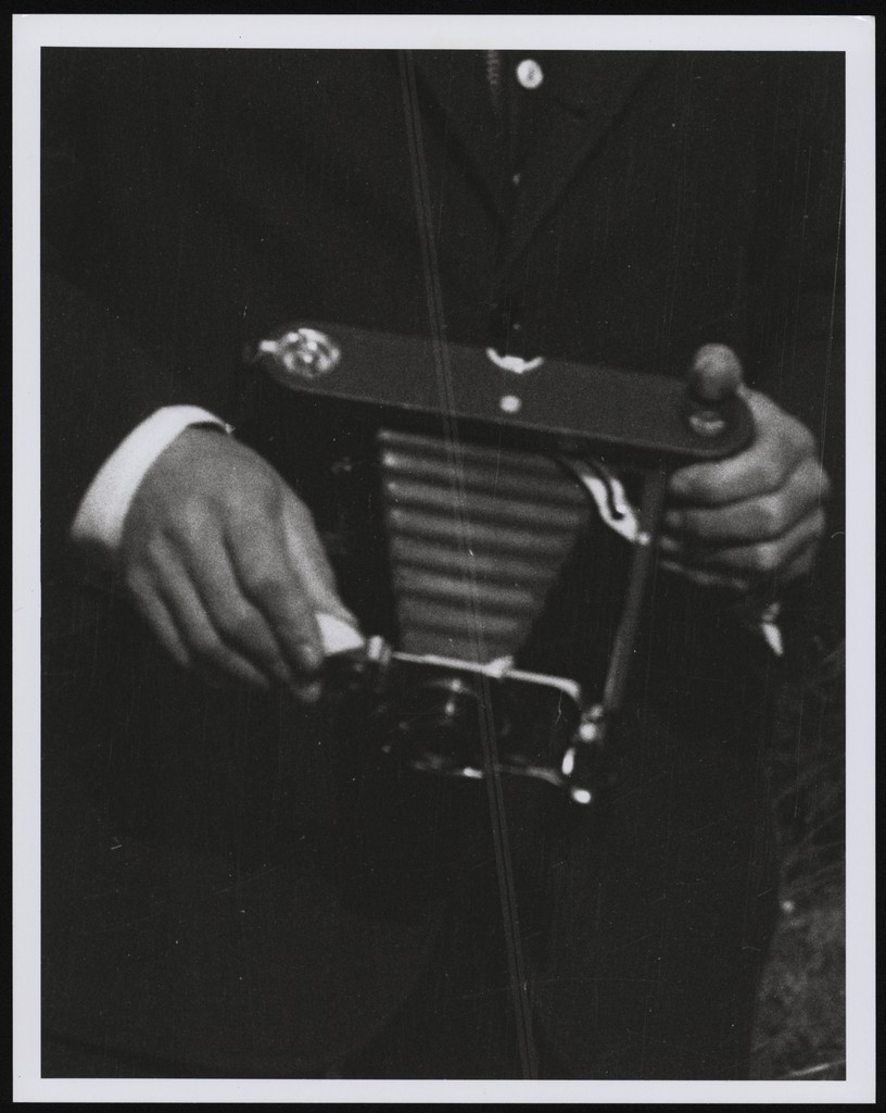 A detail of a photograph of men’s hands holding a vintage camera. 