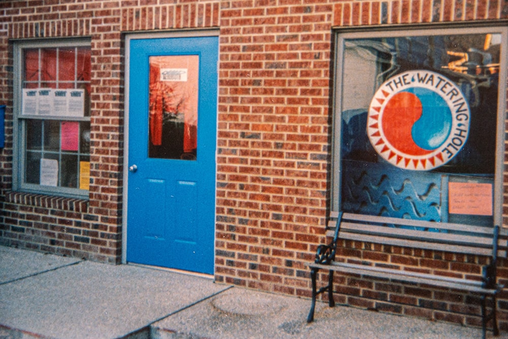 A blue door on a brick building with windows on either side.