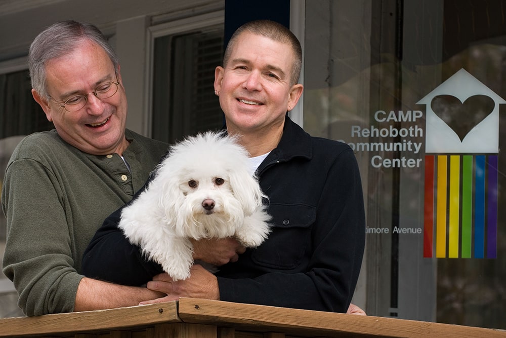 Two white men hold a small white dog together.