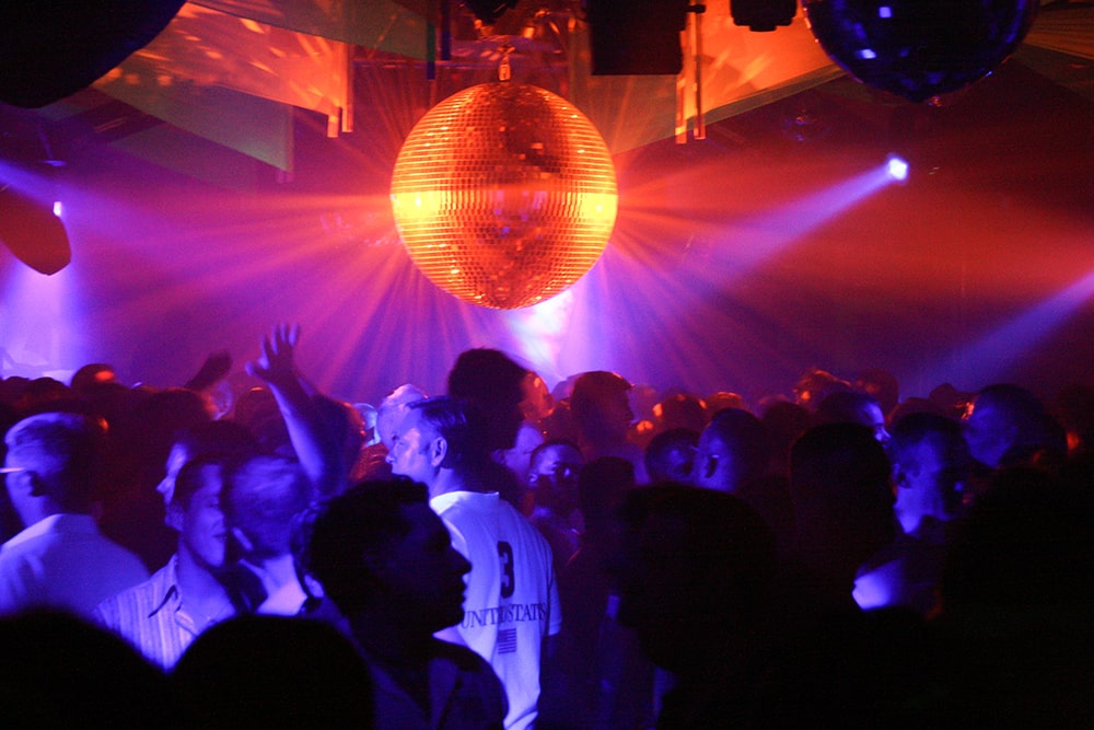 A disco ball shines over a crowd of men dancing.