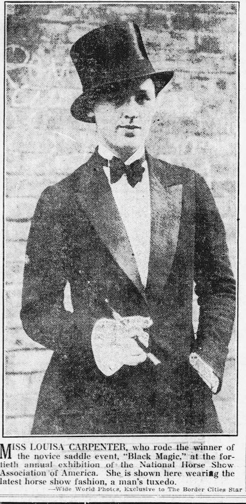 A black and white photograph of a woman posing confidently in a men’s top hat, suit and bow-tie.