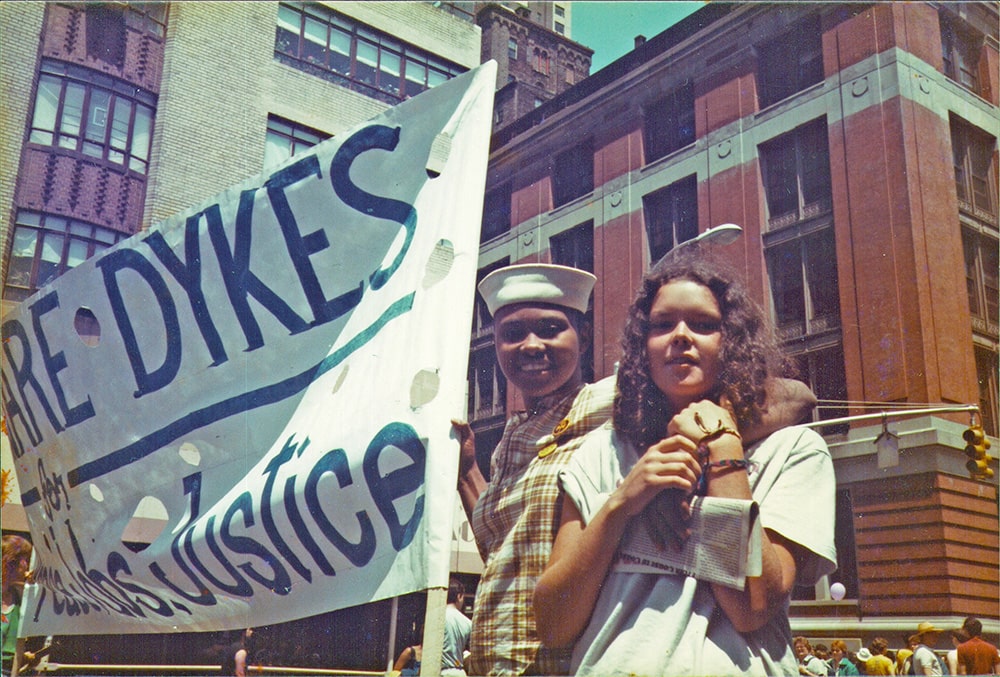 Couple stands in the street holding sign that partially reads, "Delaware Dykes".