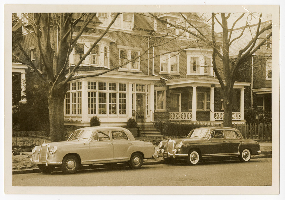 A street with two homes and two vintage cars visible.