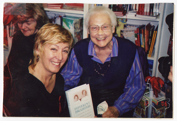 Two white women, one elderly and one middle-aged, pose with a book inside of a bookstore.