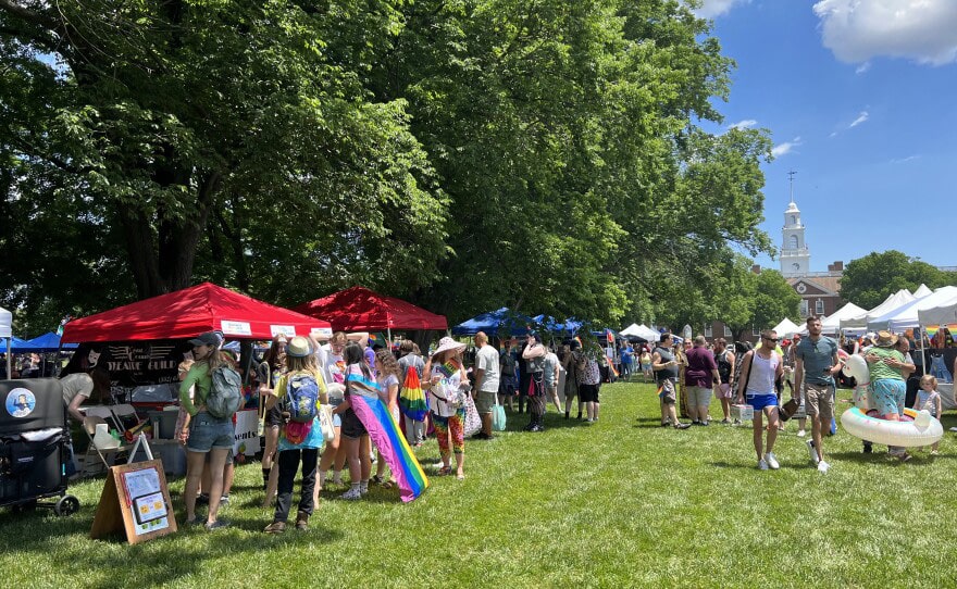 Crowds of people are seen walking the green, visiting vendors under tents. Legislative Hall is visible in the background.