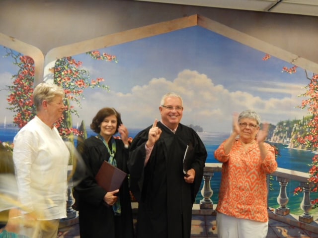 Four people pose for a picture inside the Clerk of the Peace’s office. Two county officials in black robes smile at the camera.