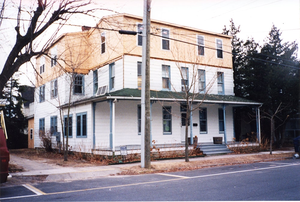 A two-story white house is seen with a third-story addition under construction.