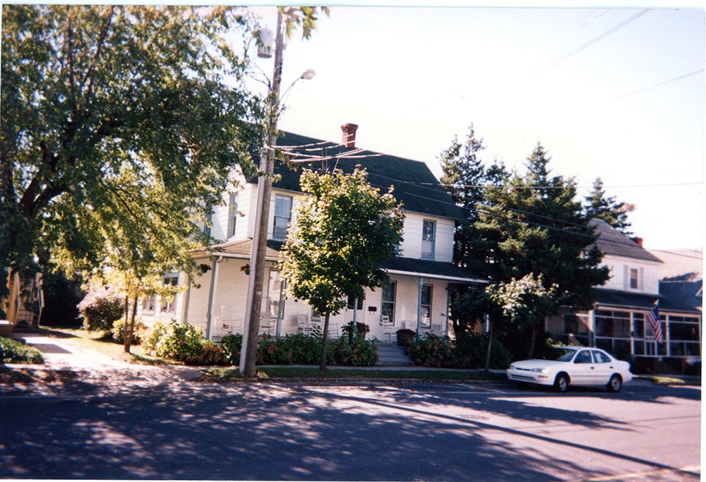 A two-story, white house with a porch is seen from across the street.