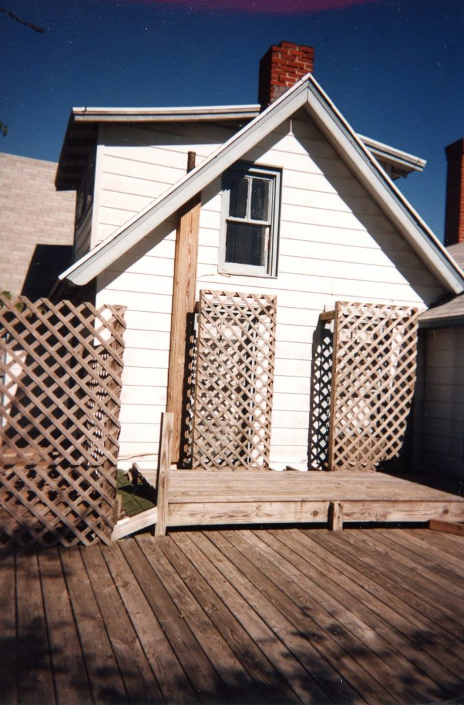 A small stage is seen on a wooden deck of a white house.