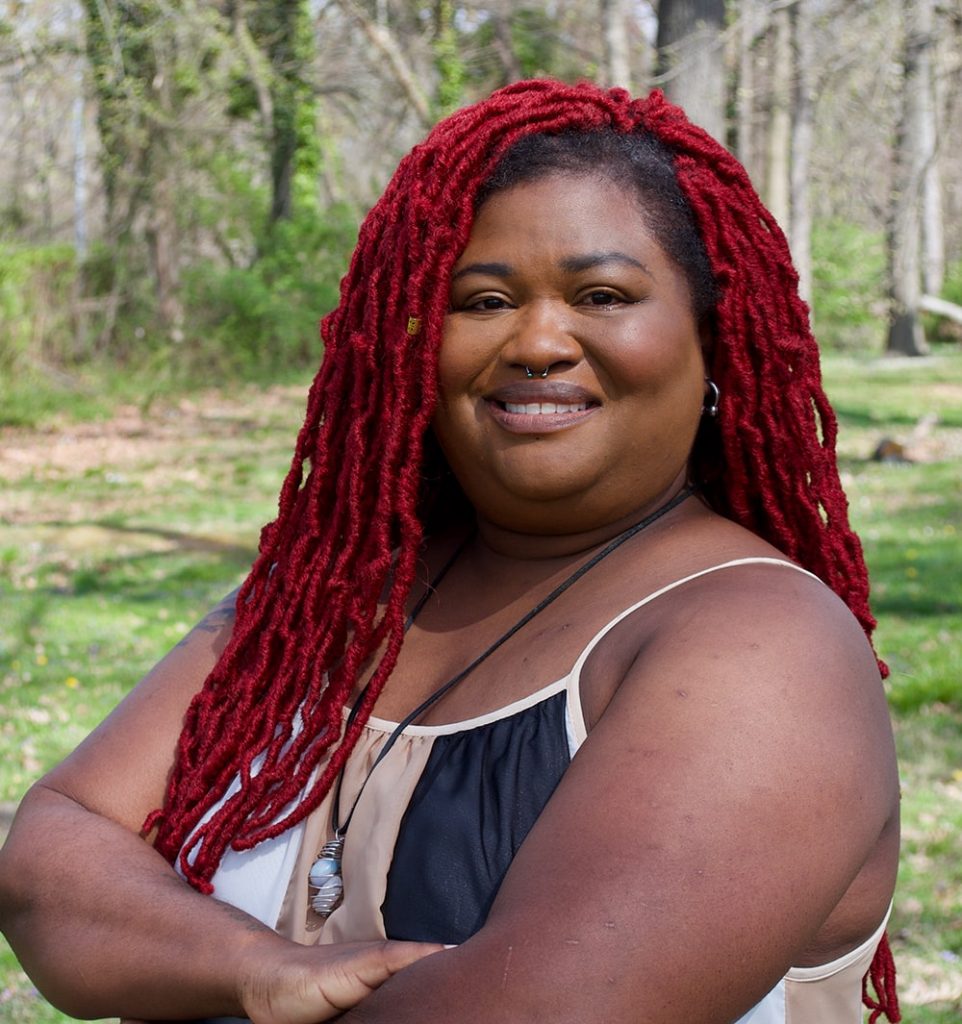 A portrait of a smiling Black woman with long red hair.