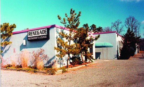 An off-white building with a hot pink roof is seen from the parking lot. A black and white sign reads “Renegade Restaurant & Lounge.”