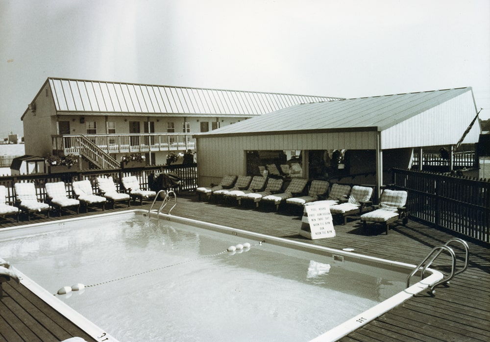 A pool with lounge chairs and an illegible sign is seen.