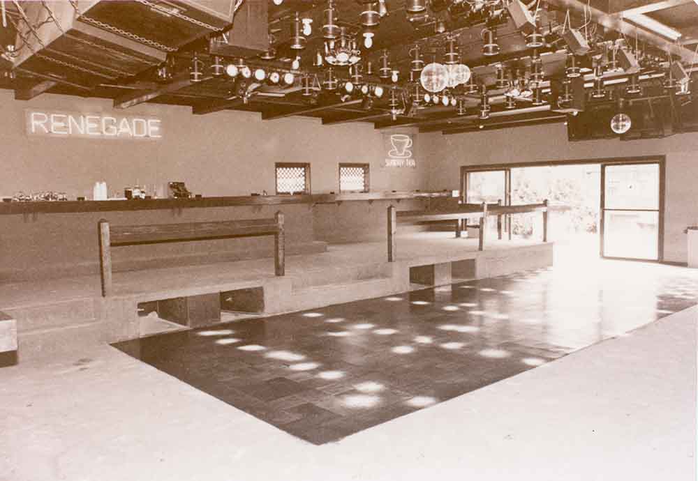 An empty dance floor with a neon sign reading “Renegade” in the background. Three disco balls are seen in the ceiling.