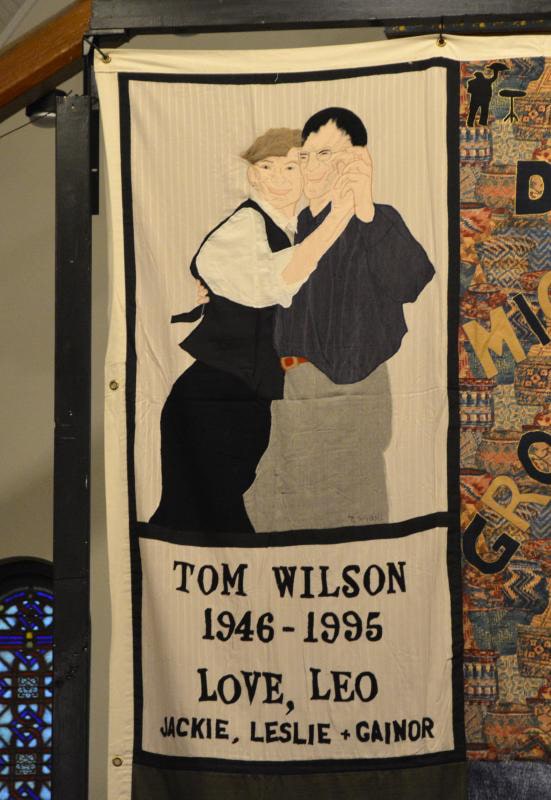 A hand-made quilt panel depicting 2 white men slow dancing.