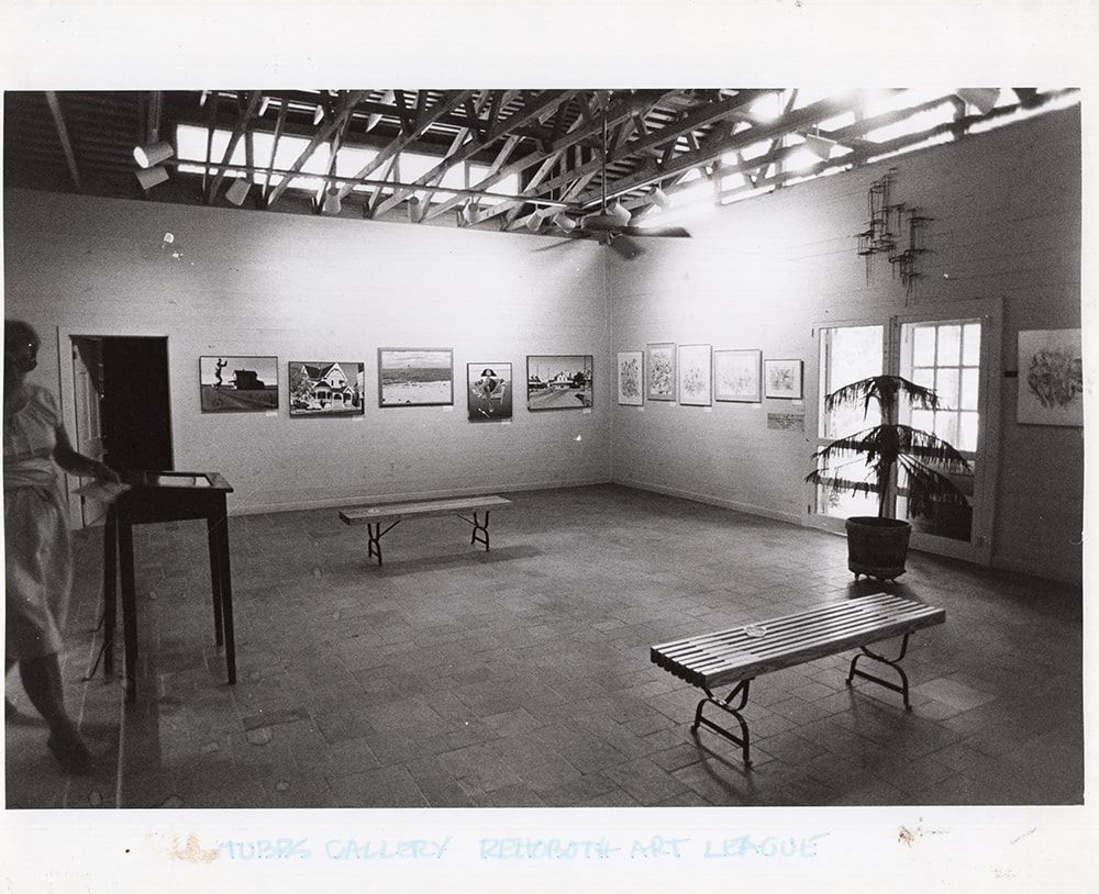 A black and white photograph of an art gallery with 5 oil paintings by Tom Wilson displayed on the wall.