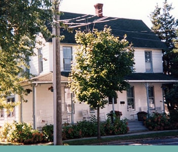 A two-story, white house with a porch is seen from across the street.
