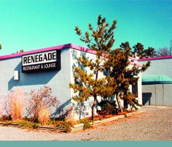 An off-white building with a hot pink roof is seen from the parking lot. A black and white sign reads “Renegade Restaurant & Lounge.”