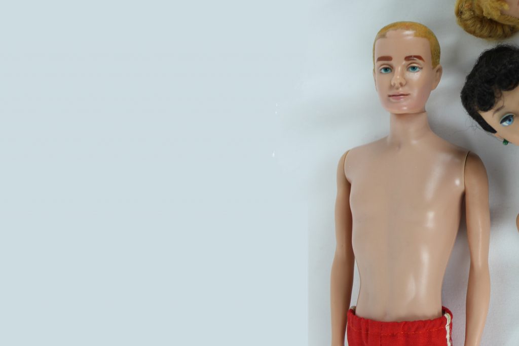 A half body shot of an original blond Ken doll wearing red swim trunks