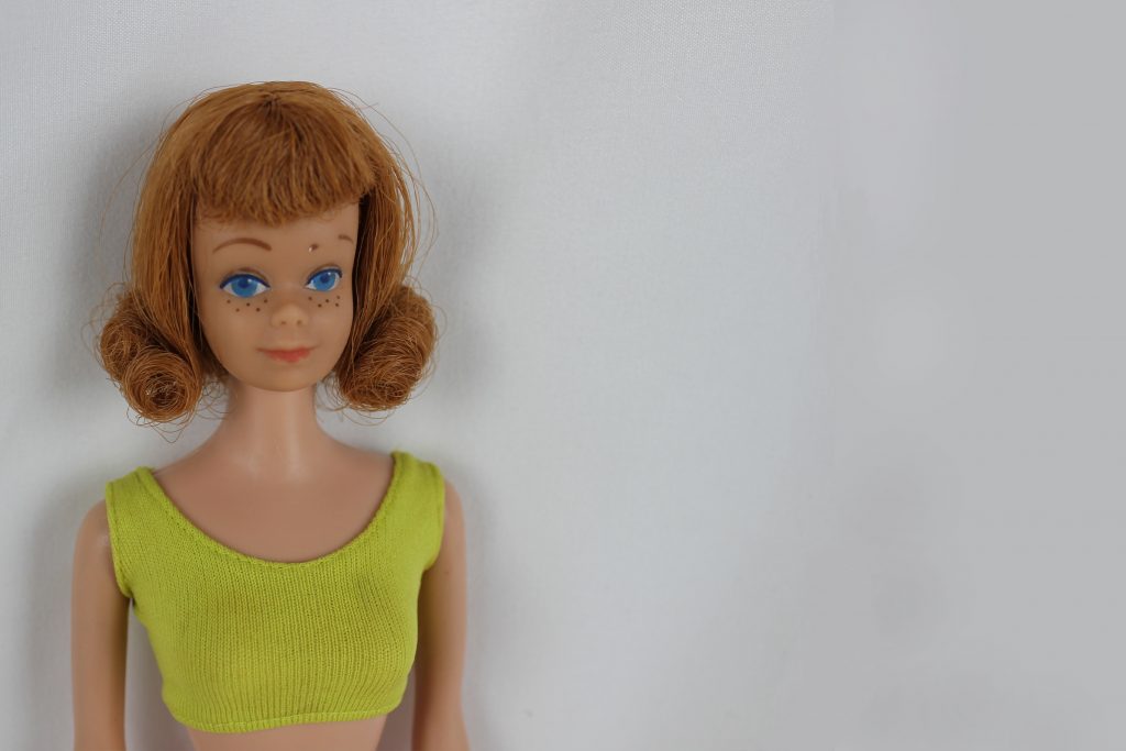 A half body shot of the original Midge doll, a short haired red-head in a green tank top.