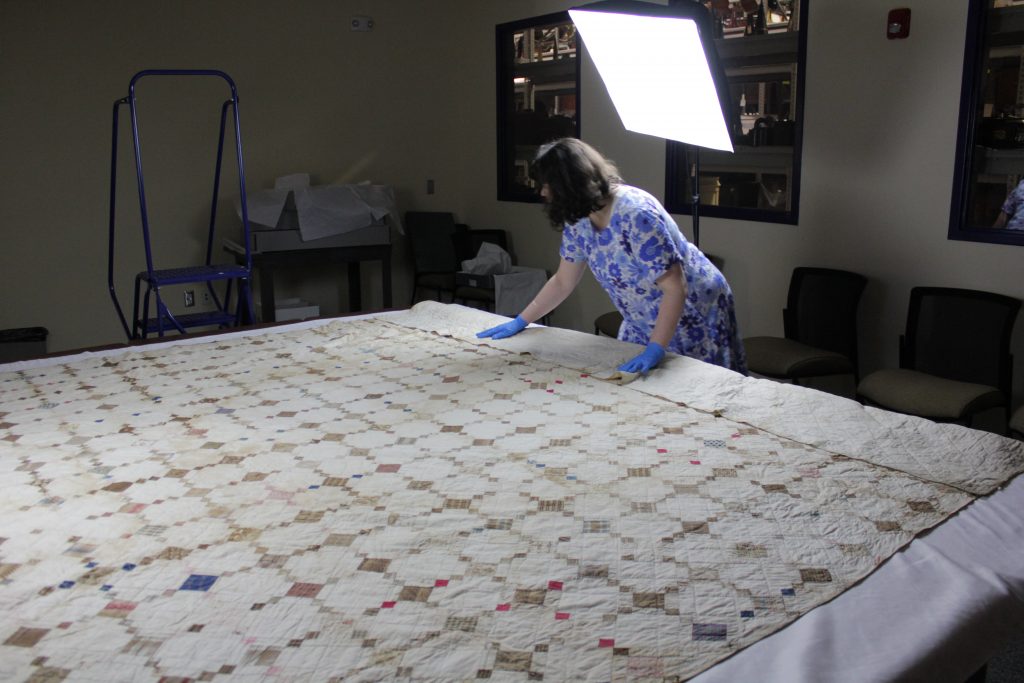 Curator Katy Little unfolding and adjusting large quilt