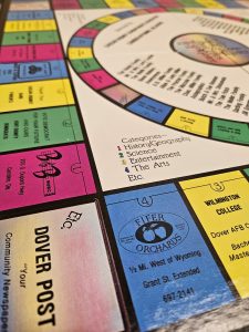 A Monopoly-like board game is shown with spaces featuring Dover-area businesses like Dover Post, Fifer Orchards and Wilmington College.