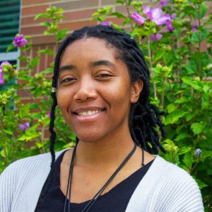 Portrait of Jordyn Willis smiling at the camera with flowers behind them.