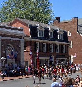 Exterior street view of Historic New Castle and a parade of people in colonial clothing carrying flags, muskets and drums in celebration of Separation Day.