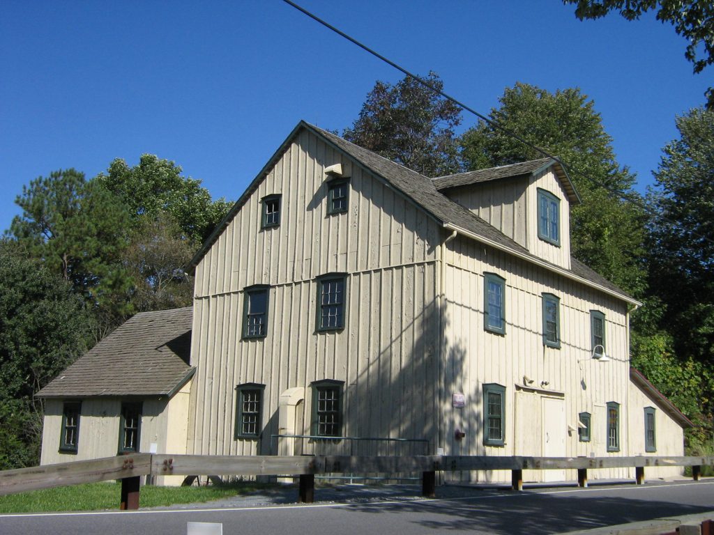 Long, exterior view of beige-colored three-story Mill with pitched roof lines and dormer window.