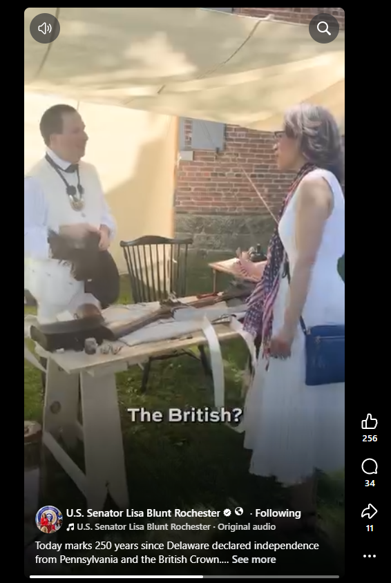 Man in British Loyalist attire of white clothing holds his black hat and discusses loyalist armaments and equipment with woman in white dress.
