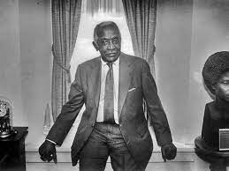 Distinguished black man in suit and tie sits upon a windowsill.
