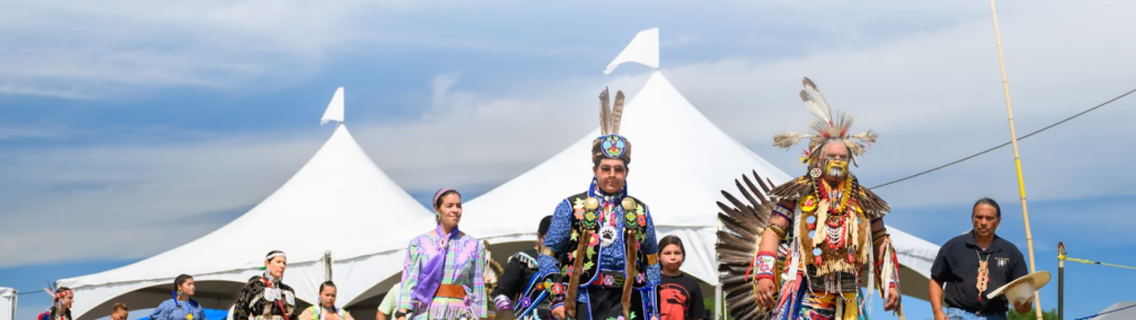 Exterior of Nanticoke tribespeople in traditional garb with white tents in the background.
