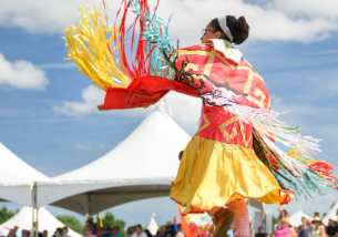 Native American woman dances outside wearing ceremonial dress and twirls to show off festive ribbon work.