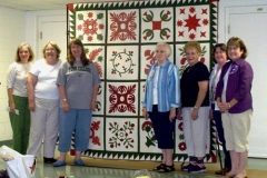 Women posing in front of quilt